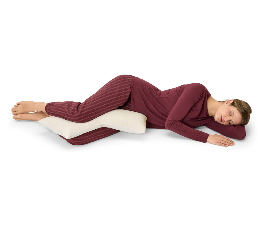 Žena leží na boku a objímá polštář.