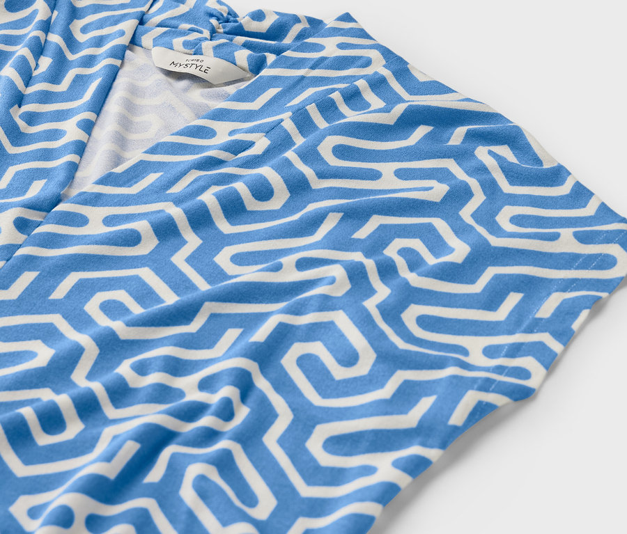 Detail modrého halenkového trika s véčkovým výstřihem a bílým geometrickým vzorem.