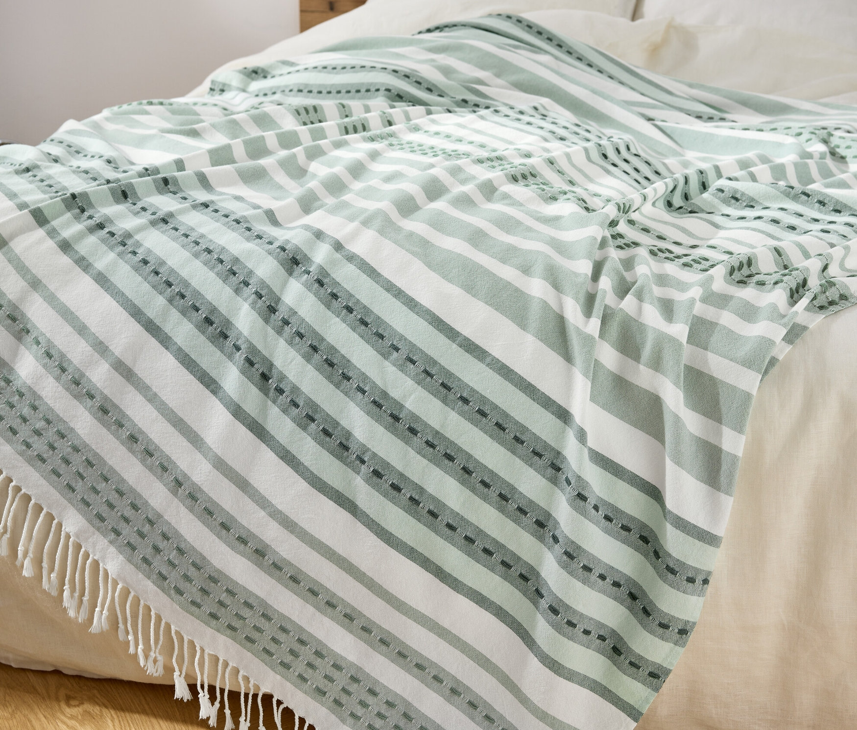 Na posteli leží pléd se zelenými a bílými pruhy a třásněmi.