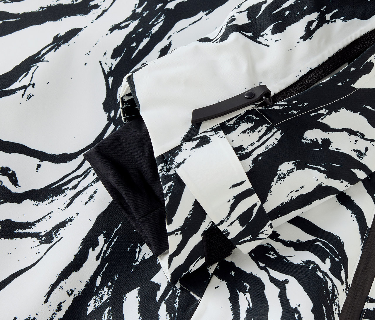 Detail bundy se vzorem zebry s bílými a černými pruhy, viditelný rukáv a zip.