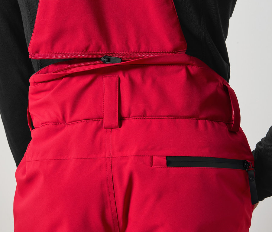 Detail červených kalhot s laclem a černým zipem.