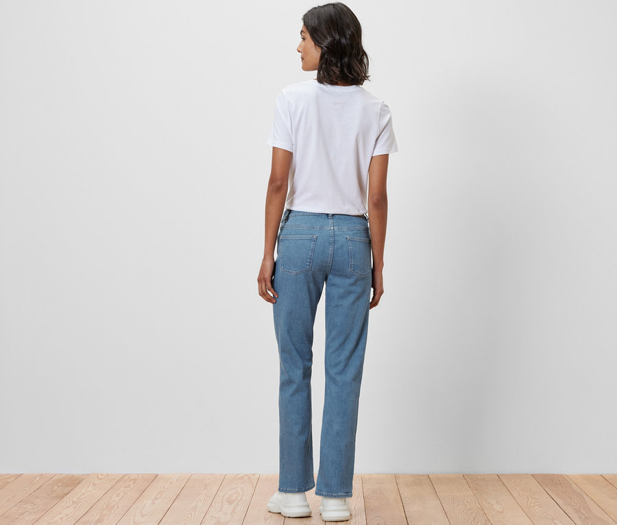 Žena stojí zády k fotoaparátu a má na sobě džíny rovného střihu »Kira« a bílé tričko.