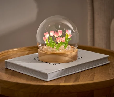 LED-DIY-Bastel-Set s tulipány ve skleněné kupoli na knize na kulatém stolku.