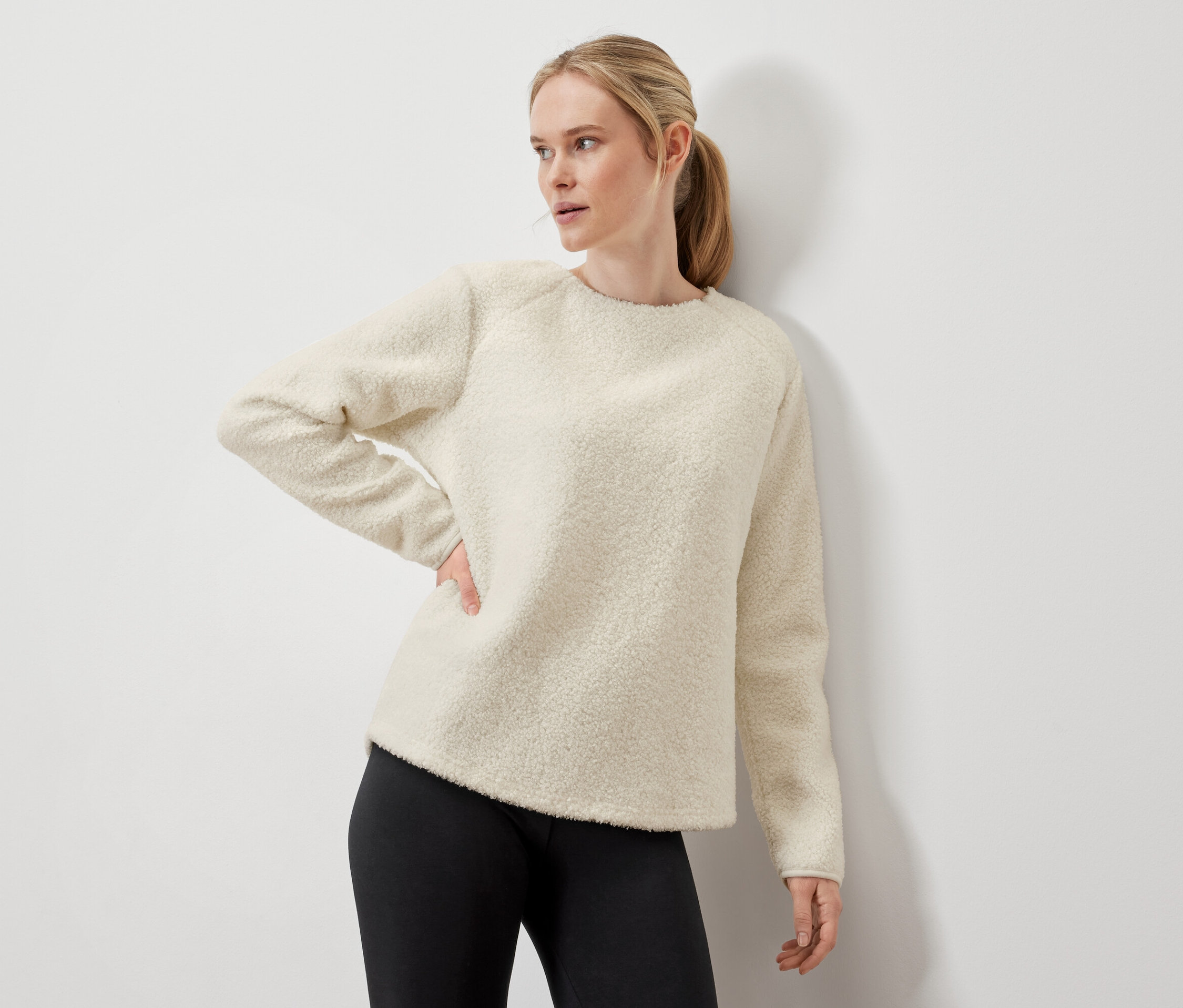 Žena pózuje v krémovém svetru a černých legínách.