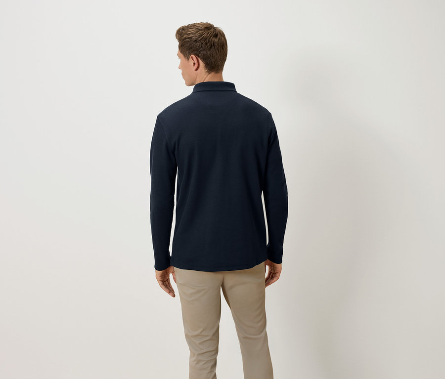 Muž zády k fotoaparátu má na sobě tmavě modré polo tričko s dlouhým rukávem a béžové kalhoty.