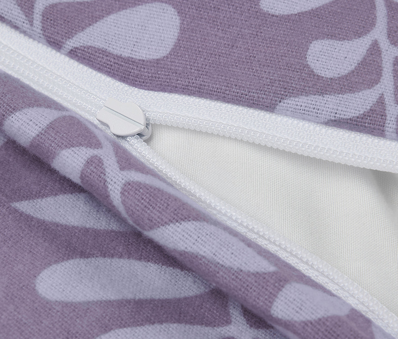 Detail fialového povlaku na polštář s bílými listy a zipem.