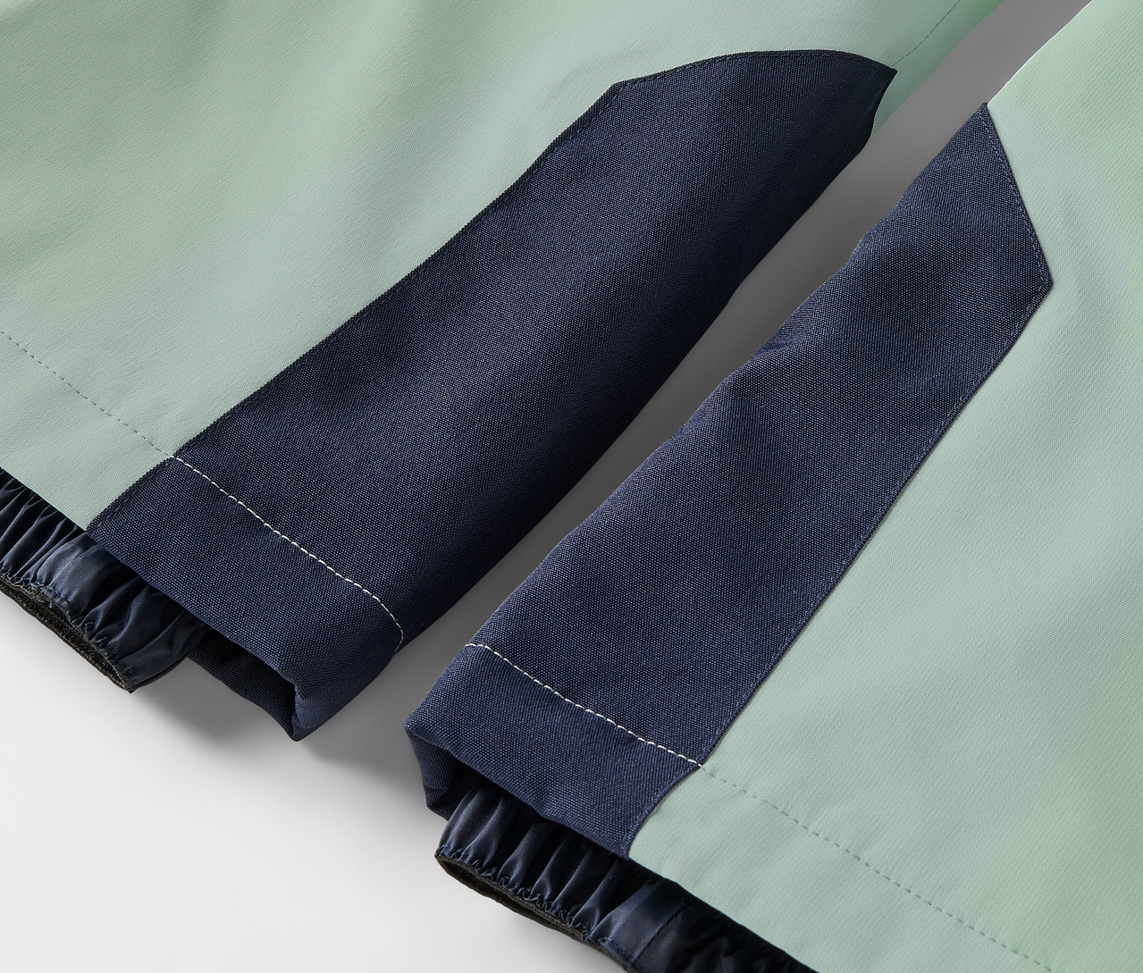 Detail světle zelené bundy s tmavě modrými rukávy a elastickými manžetami.