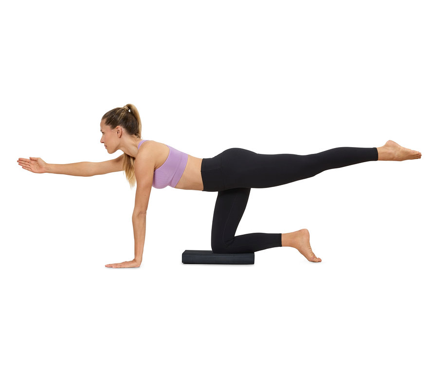 Žena cvičí jógu na podložce, má na sobě sportovní oblečení.