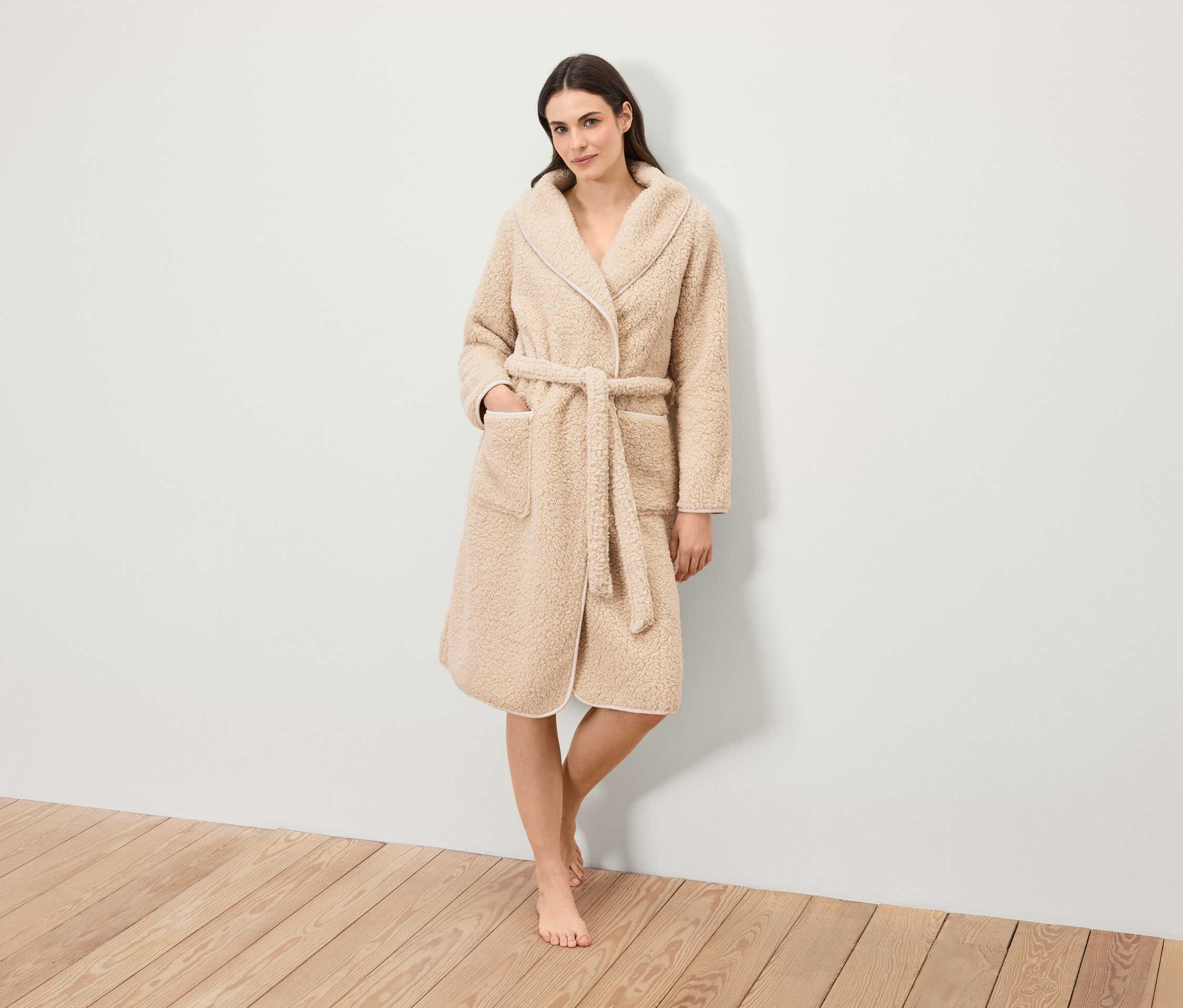 Žena stojí a má na sobě huňatý župan s páskem.