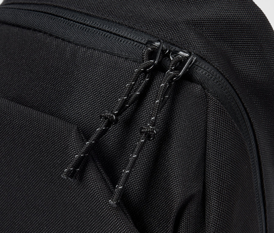 Detailní záběr na černý batoh se zipem a stahovací šňůrkou.