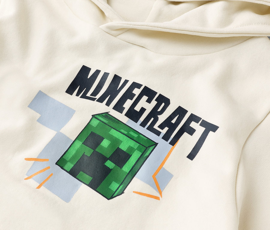 Detailní pohled na krémovou mikinu s kapucí s potiskem "Minecraft" a zeleným blokem Creeper.