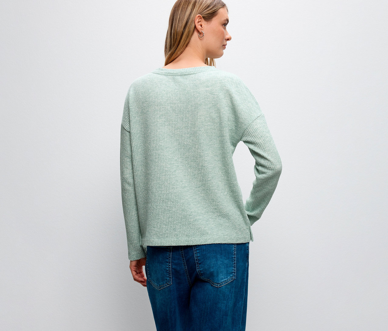 Pohled zezadu na ženu s blond vlasy v strukturovaném tričku Street One a modrých džínách.
