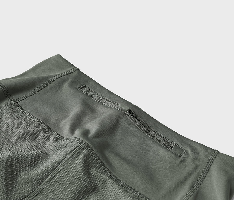 Detailní záběr olivově zelených kalhot s kapsou na zip.