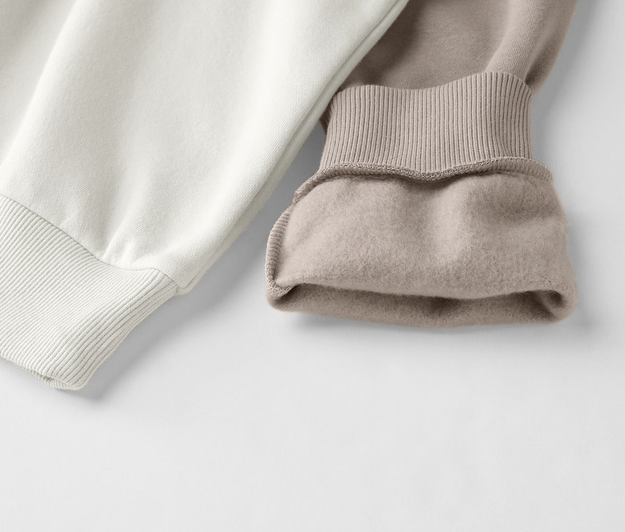 Detailní záběr na dvoubarevnou mikinu v bílé a béžové barvě s žebrovanými manžetami.