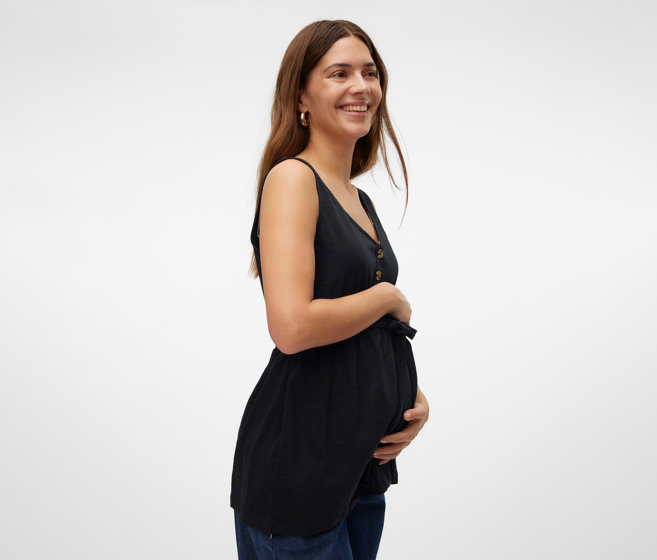 Usmívající se žena drží si břicho a má na sobě černé kojící tílko MAMALICIOUS »MLEVI LIA« a džíny.