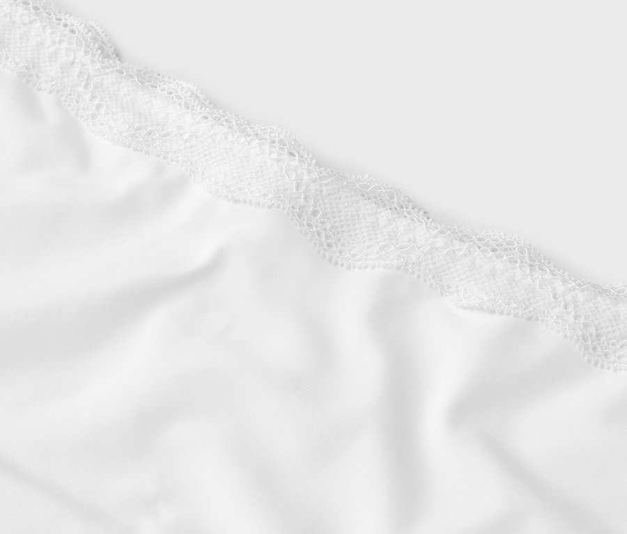 Detailní pohled na bílou látku s bílou krajkou nahoře.