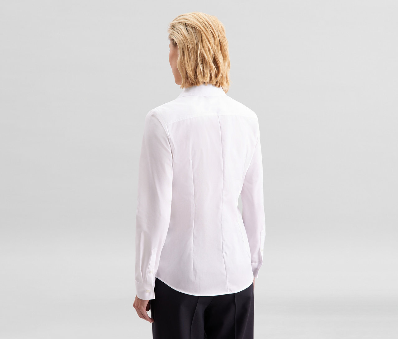 Žena zezadu, oblečená v bílé halence slim fit non iron Seidensticker a černých kalhotách.