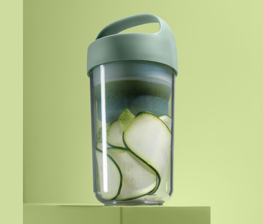 Cestovní dóza na oběd se zeleninou na zeleném podstavci.