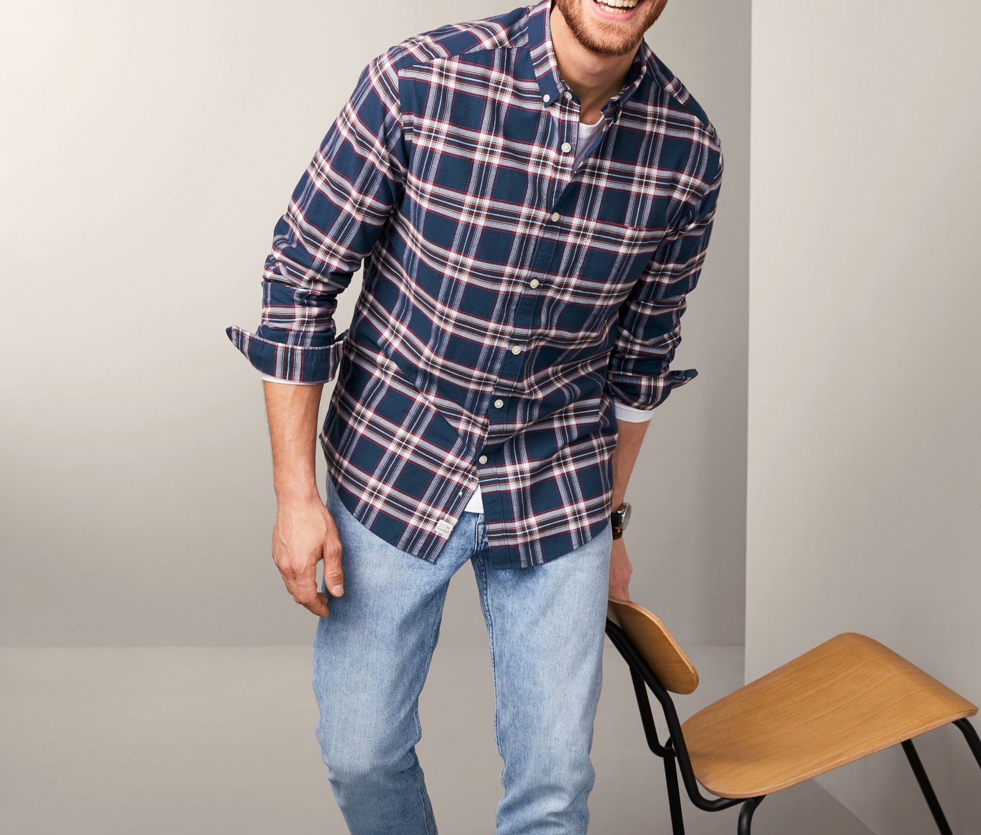 Muž se usmívá a pózuje v modré kostkované flanelové košili.
