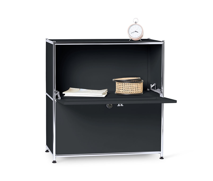 Černá kovová odkládací skříňka CN3 s výklopnými dvířky, na níž leží budík, košík a papíry.