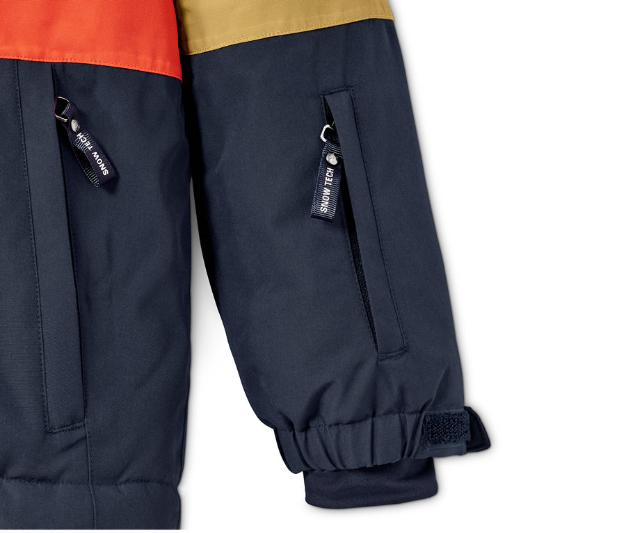 Detail snowboardové bundy s oranžovým a hnědým blokem barev a kapsami na zip.