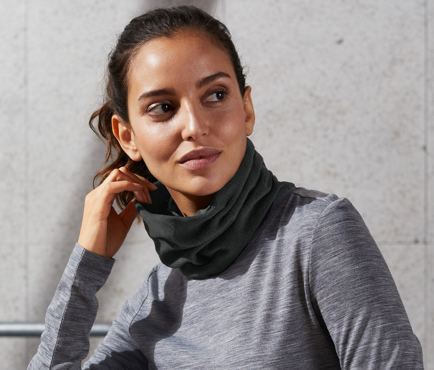 Žena sedí a nosí multifunkční šálu/čepici kolem krku.