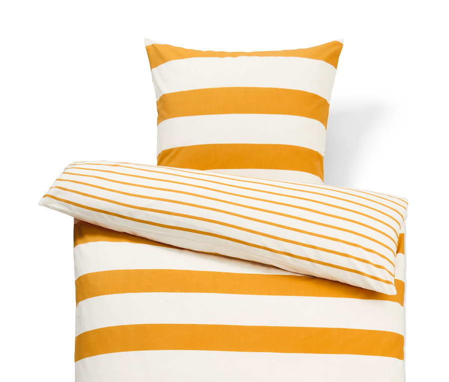 Pohled shora na ložní soupravu: přikrývka a dva polštáře s oranžovými a bílými vodorovnými pruhy.