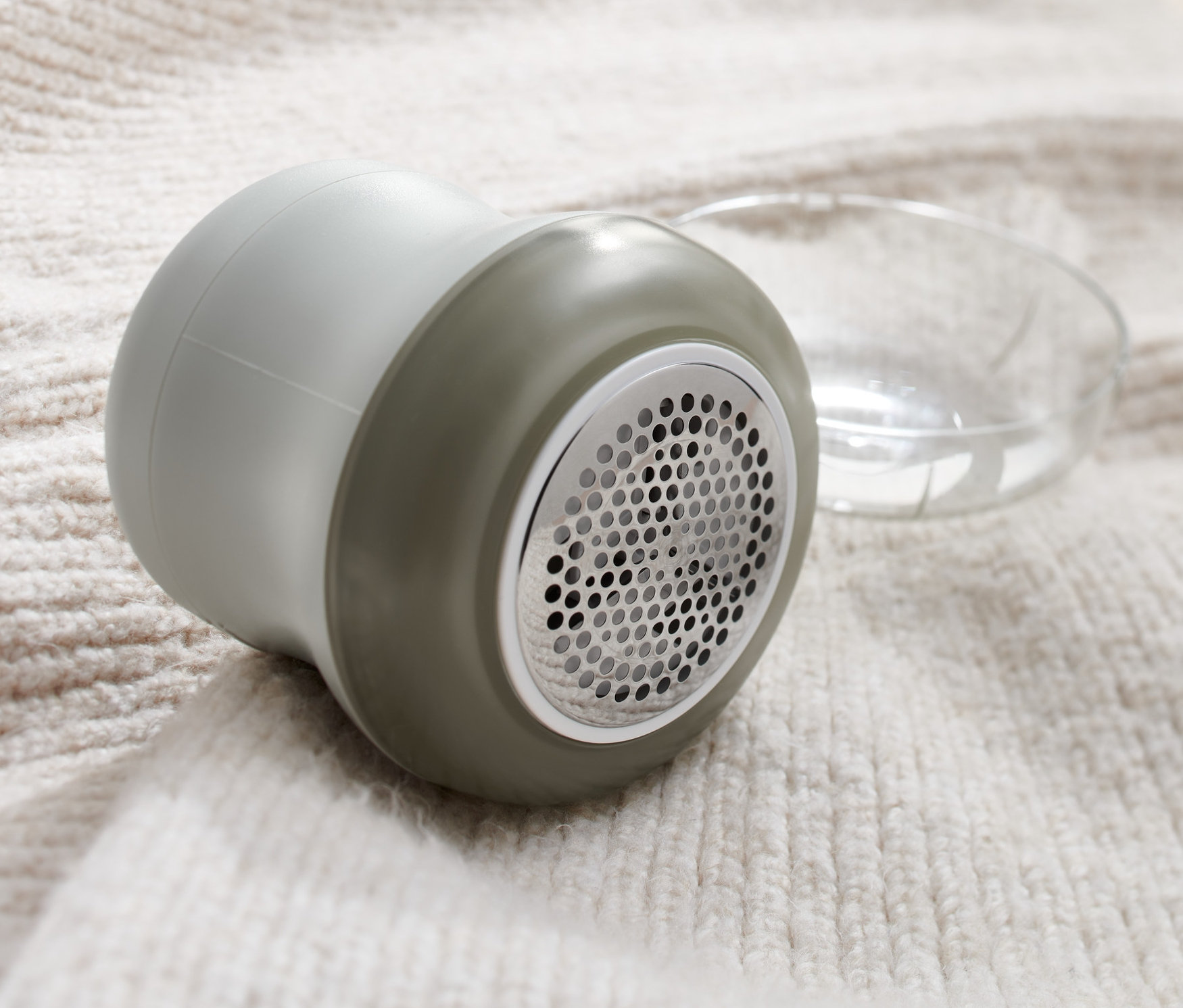 Šedý odstraňovač žmolků leží na svetru.