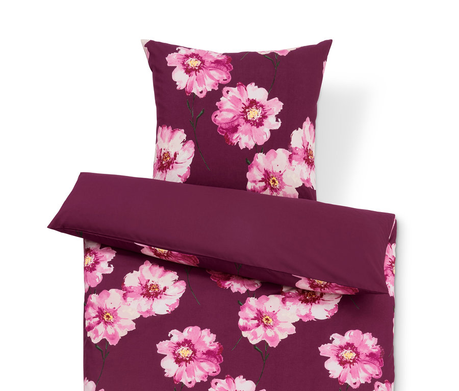 Fialové povlečení s květinovým vzorem a jednobarevný fialový polštář.