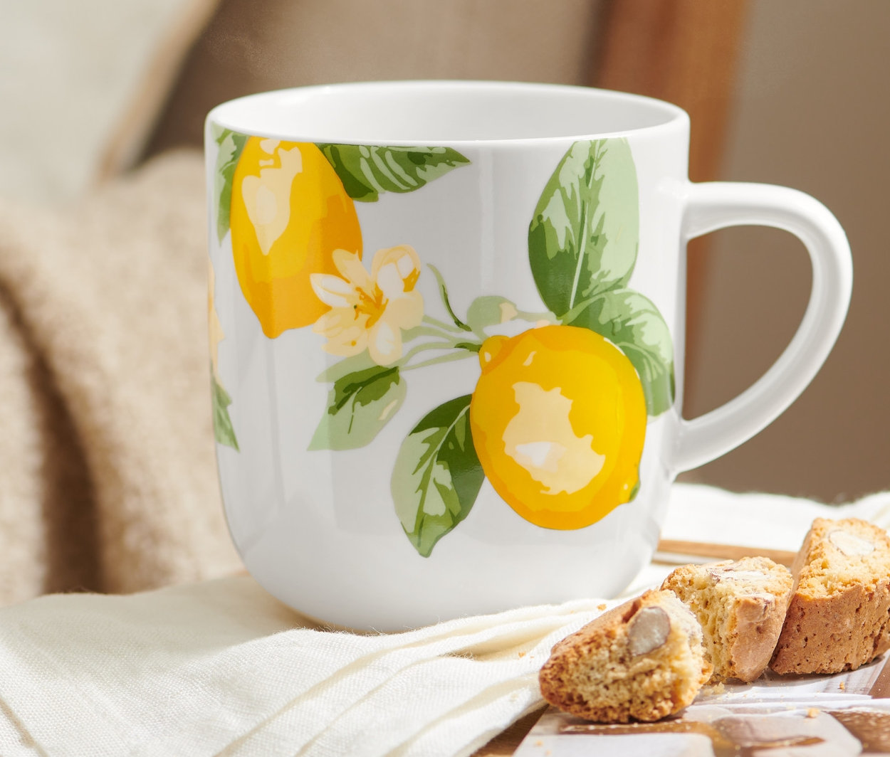 Na dřevěné židli leží Velký hrnek s motivem citronů, vedle něj leží bílý ubrousek a sušenky.