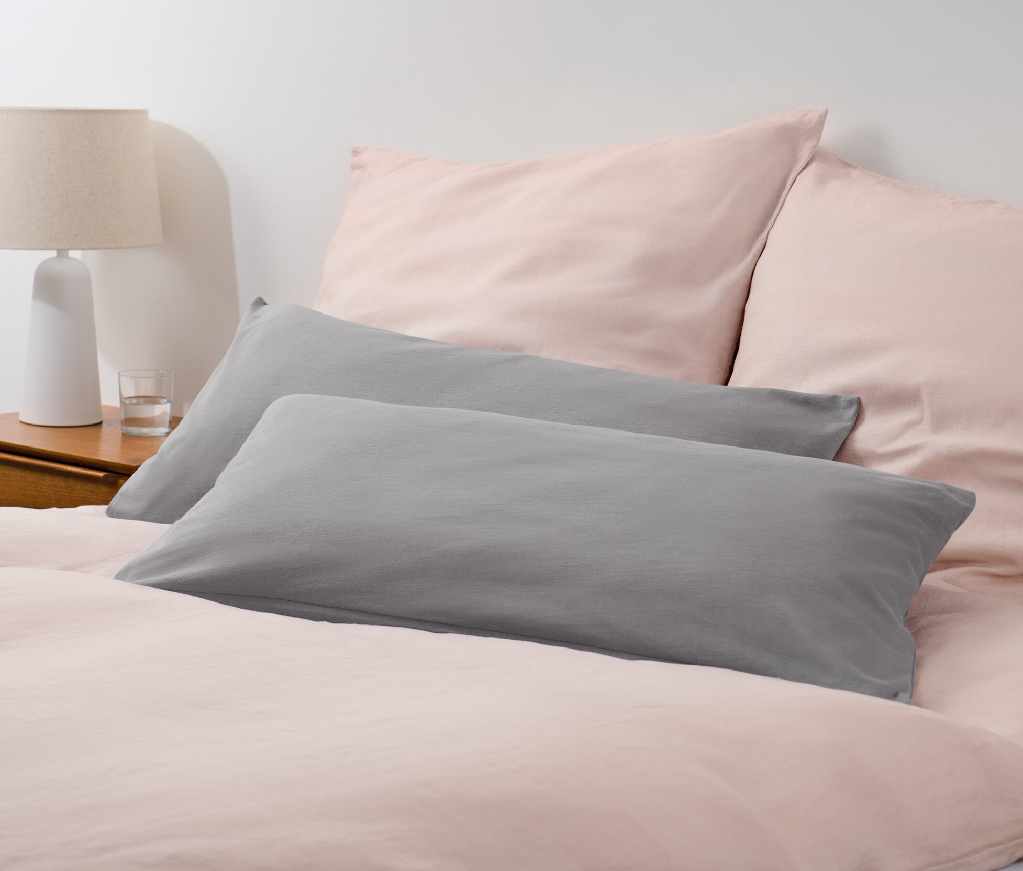 Dva šedé žerzejové povlaky na polštáře na posteli s růžovým ložním prádlem.