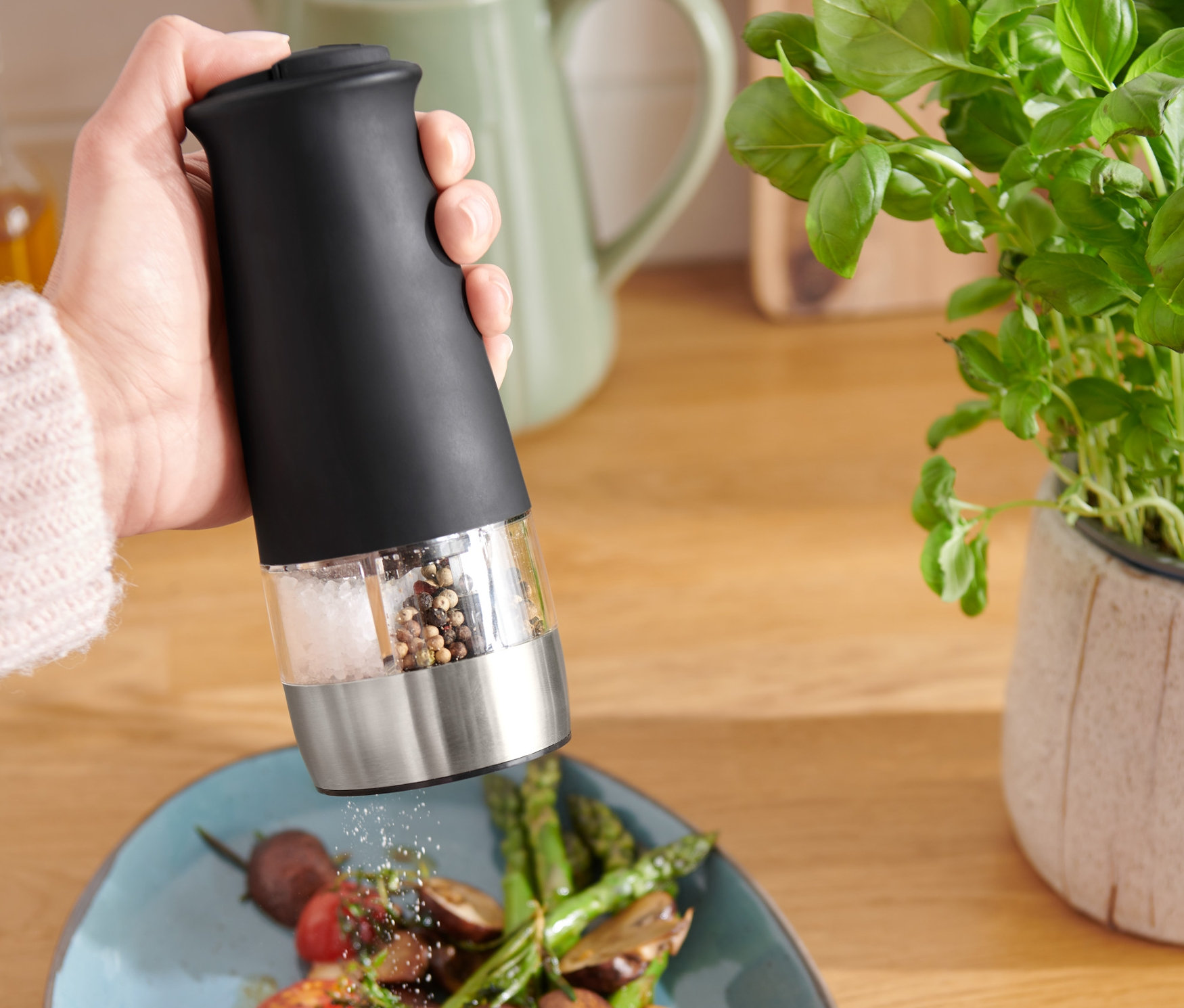 Osoba používá elektrický mlýnek na sůl a pepř 2 v 1 na talíř se zeleninou.