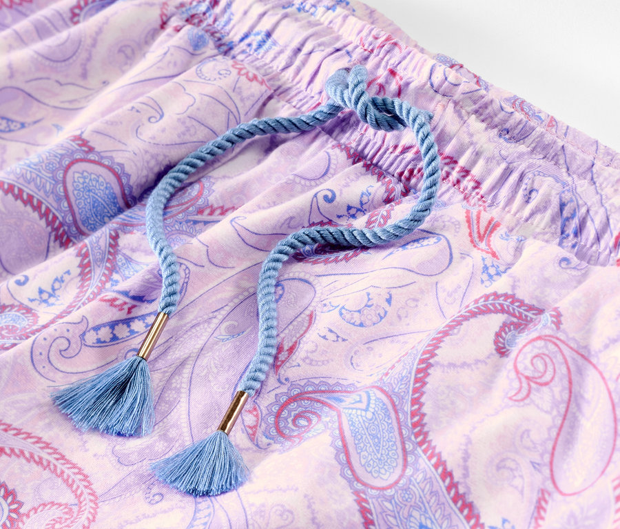 Detail fialových pyžamových kalhot s paisley vzorem a modrou stahovací šňůrkou.