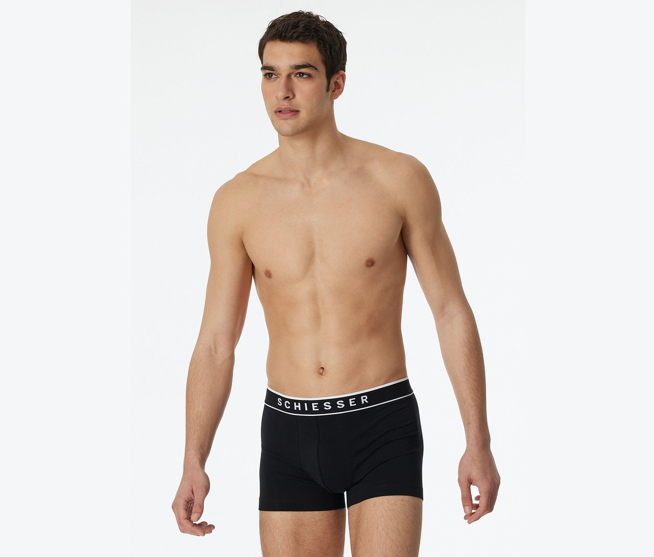 Muž bez trička pózuje v černých boxerkách Schiesser.