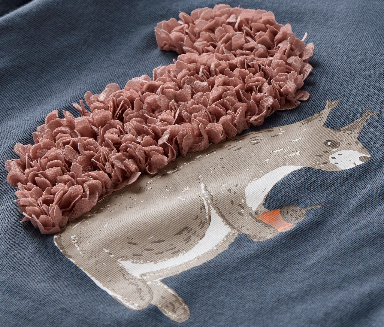 Detail modrého trička s dlouhým rukávem s 3D aplikací veverky.