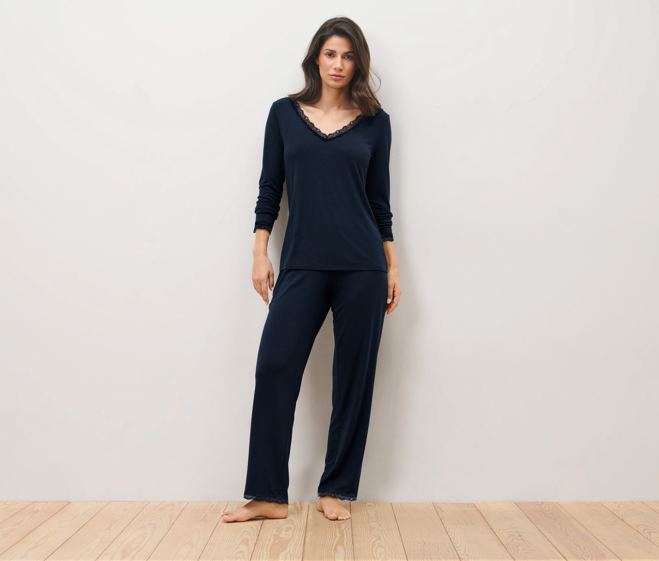 Žena stojí na dřevěné podlaze a má na sobě tmavě modré pyžamo.