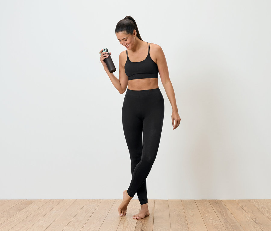 Žena v černém sportovním oblečení drží láhev na pití.