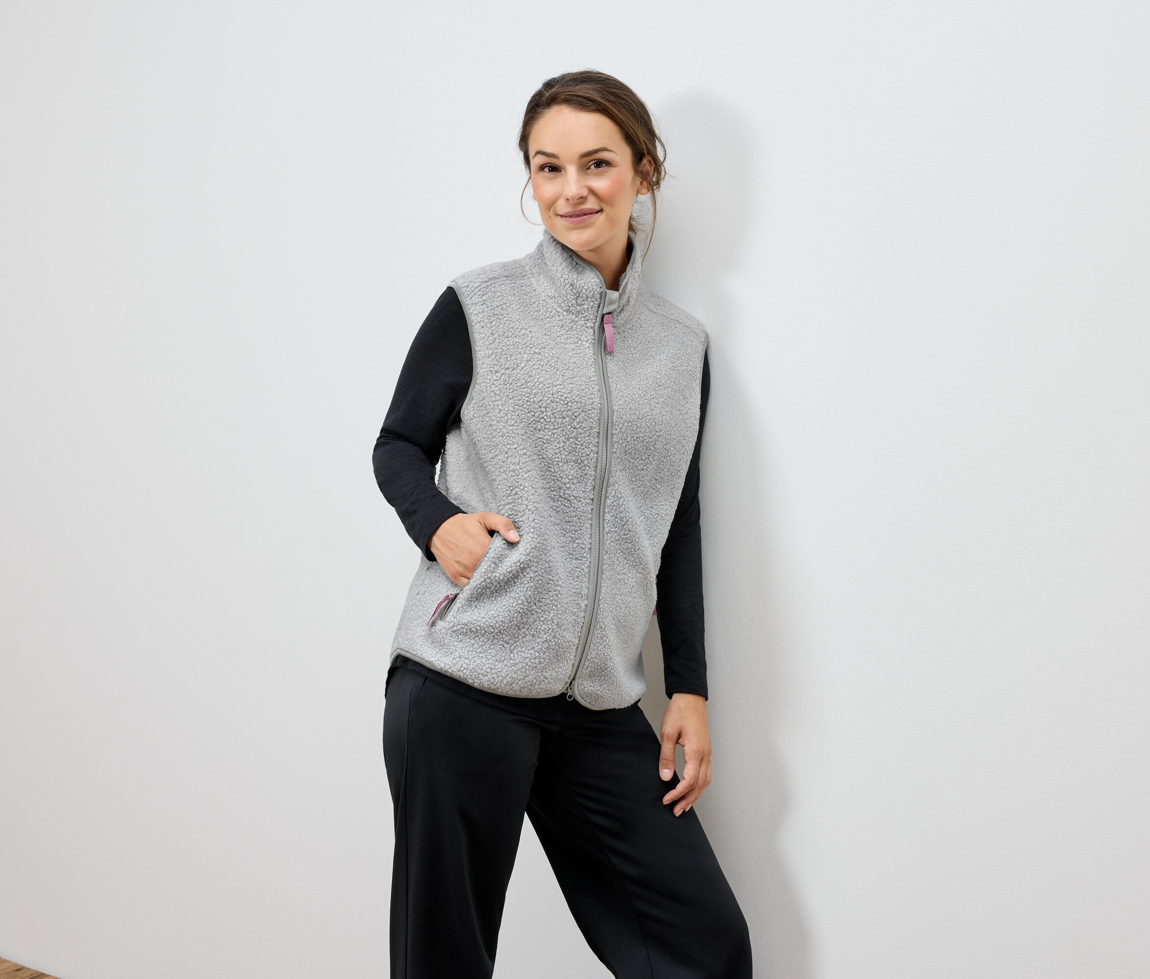 Žena má na sobě šedou fleecovou vestu a černé kalhoty.