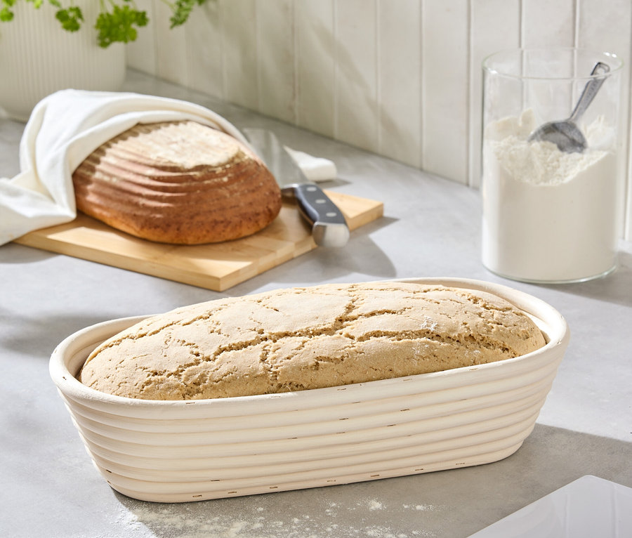 Chléb v ošatce na lince vedle mouky a chleba na prkénku.