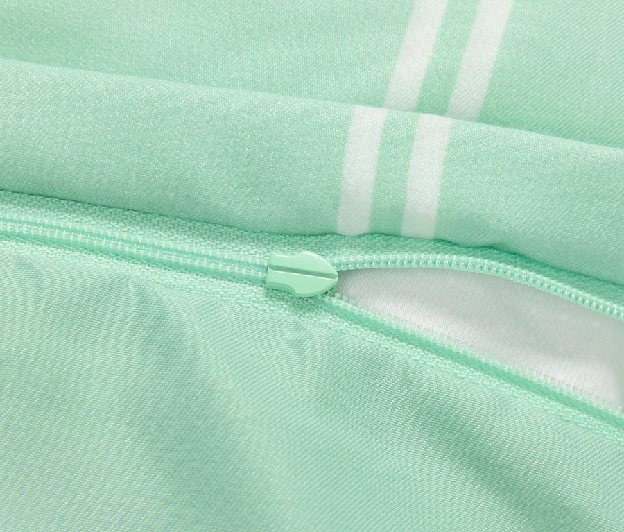 Detail světle zeleného povlečení na polštář se zipem a bílými pruhy.