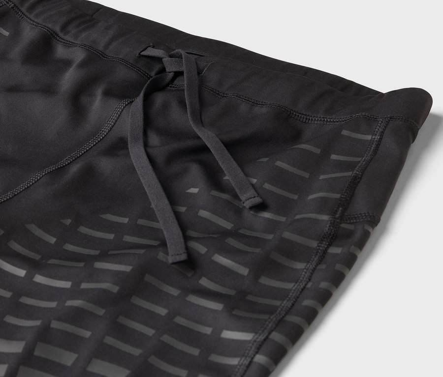 Detail černé sportovní legíny se stahovací šňůrkou a geometrickým vzorem.