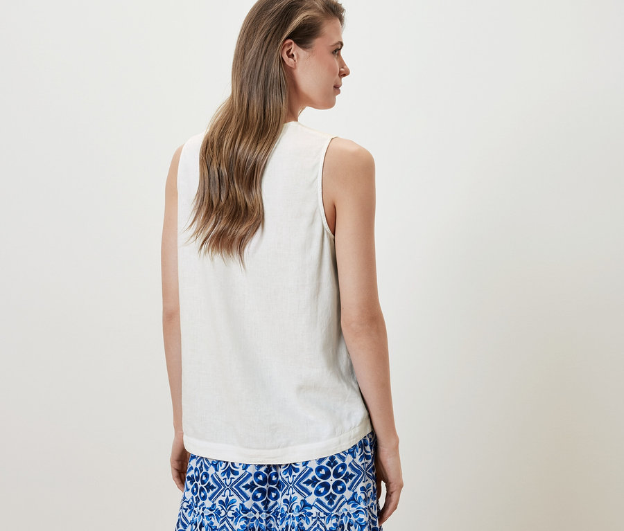 Žena má na sobě bílou lněnou halenku bez rukávů a modrou sukni.