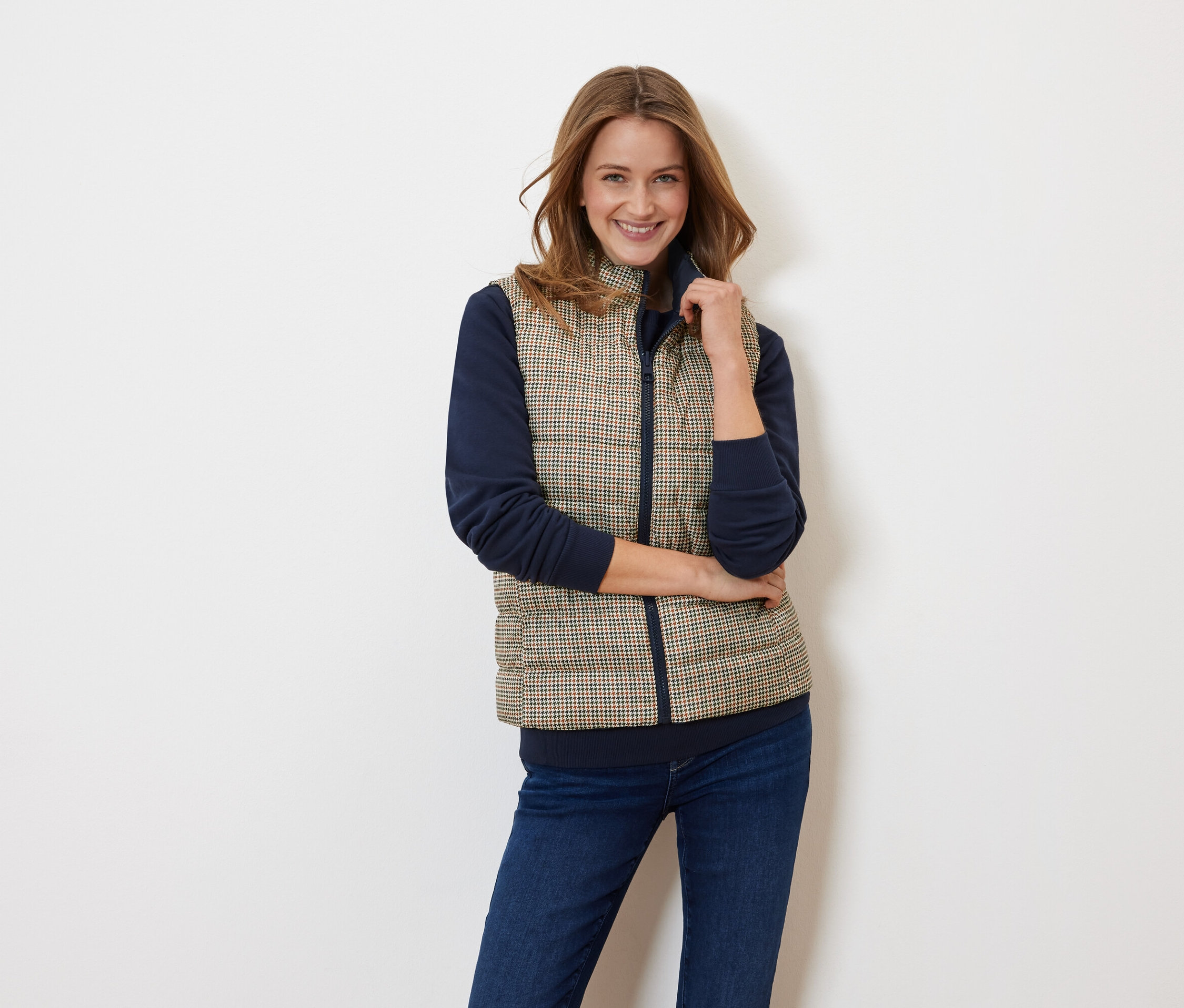 Žena pózuje na sobě prošívanou vestu a tmavě modrý top.