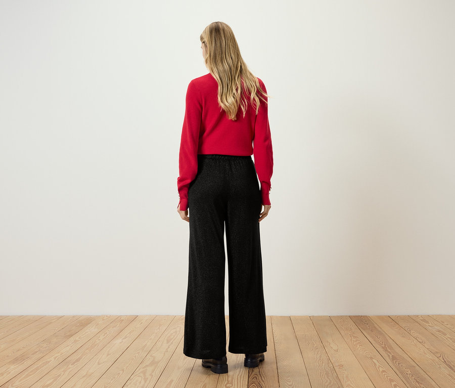 Zezadu je vidět žena s blond vlasy v červeném svetru a černých kalhotách.