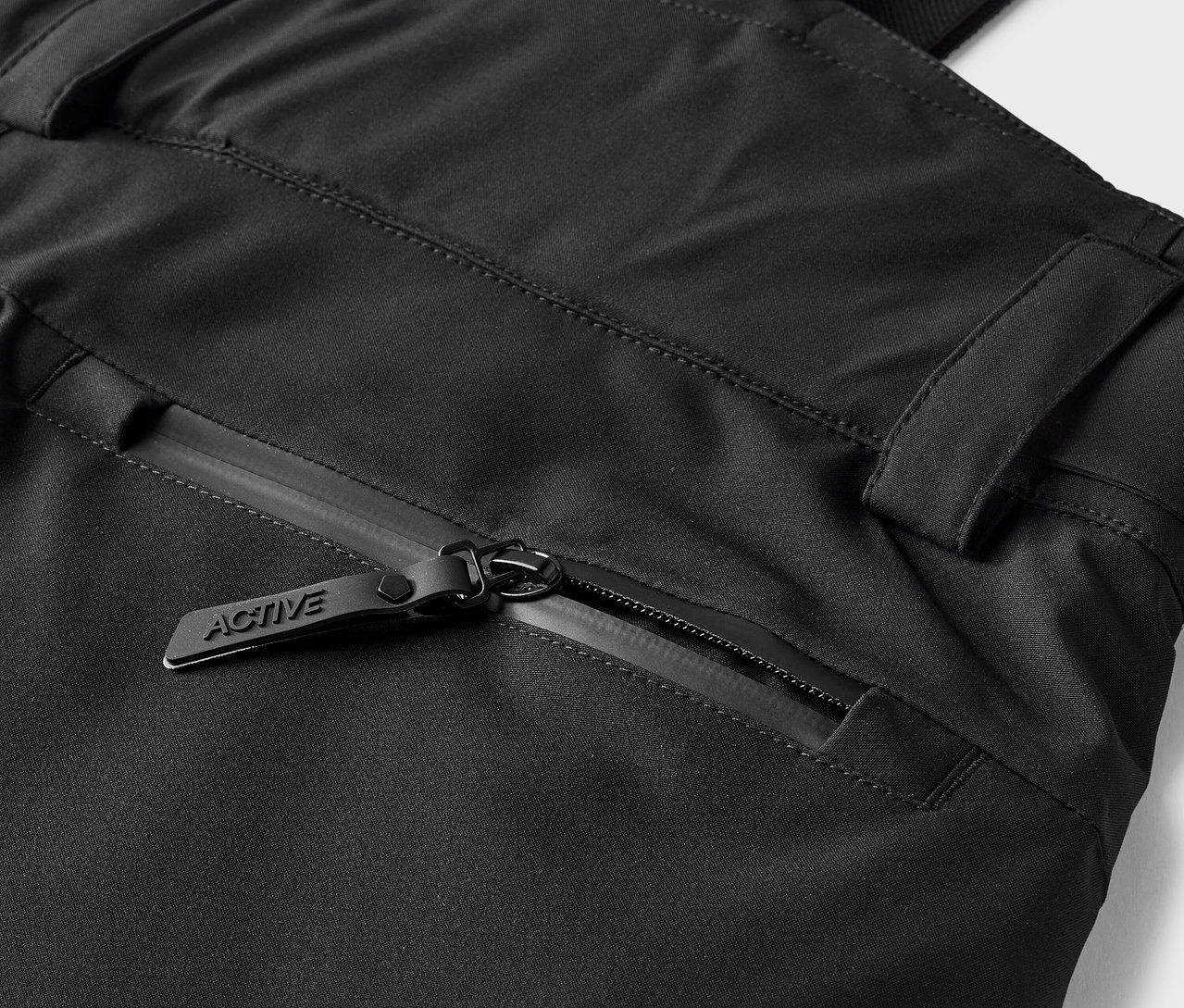 Detail černých kalhot s kapsou na zip s jezdcem s nápisem ACTIVE.