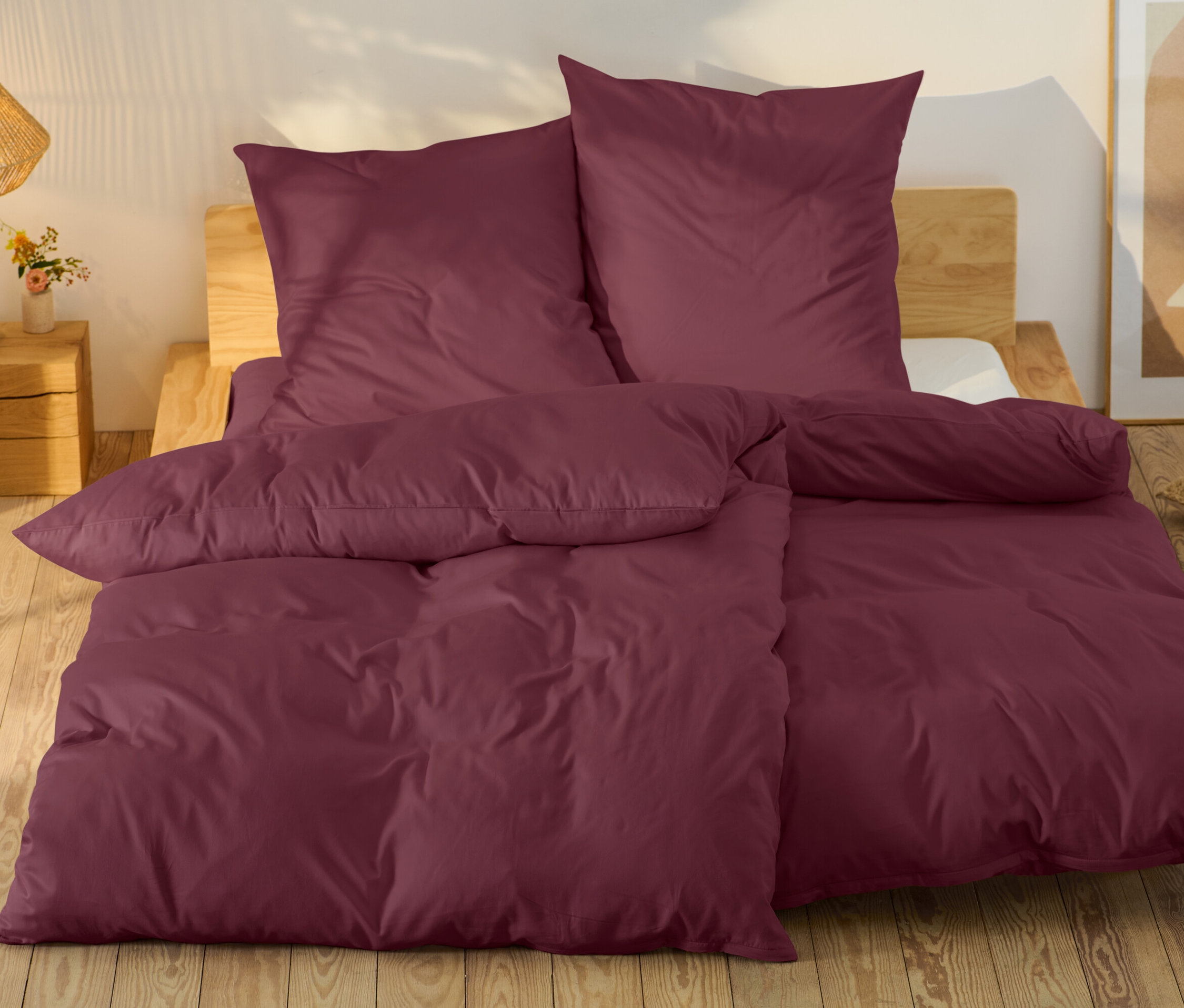 Vínové ložní prádlo na posteli s dřevěným rámem.