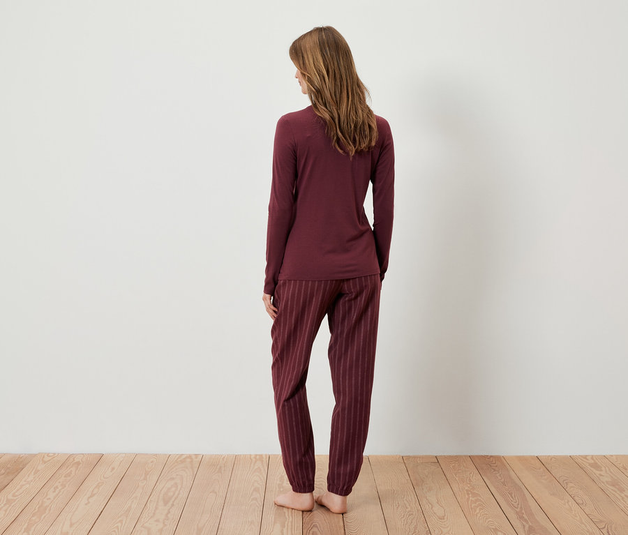 Žena stojí zády k fotoaparátu a má na sobě bordó pyžamo.