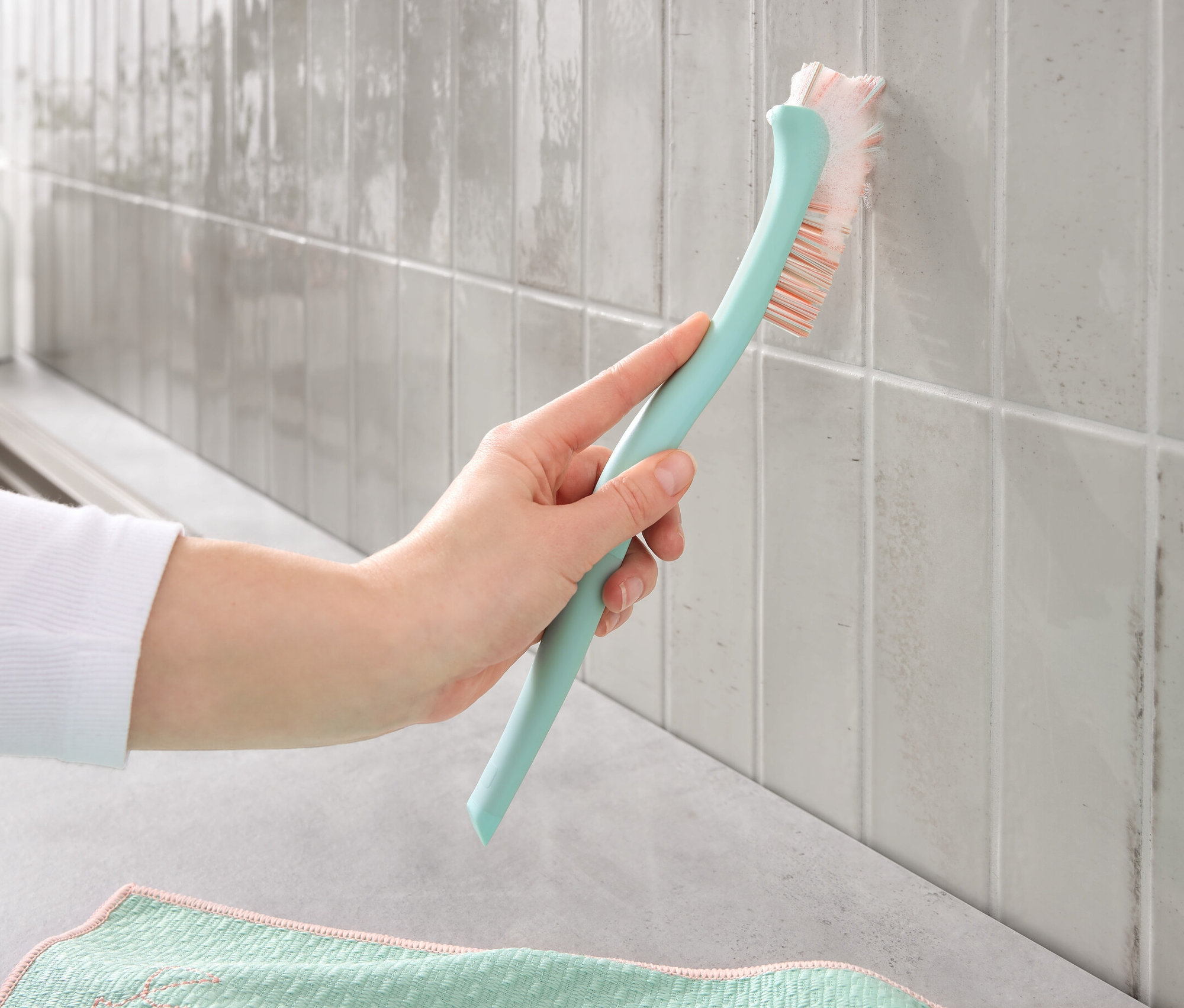 Ruka čistí Kartáčem na čištění spár špinavé spáry na dlaždicích.