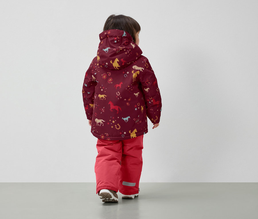Chlapec v zimní bundě s potiskem koní a červených kalhotách, zády k fotoaparátu.