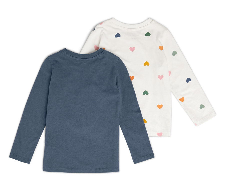 Dvě dětská trička s dlouhým rukávem. Jedno je modré a druhé bílé se vzorem srdíček.